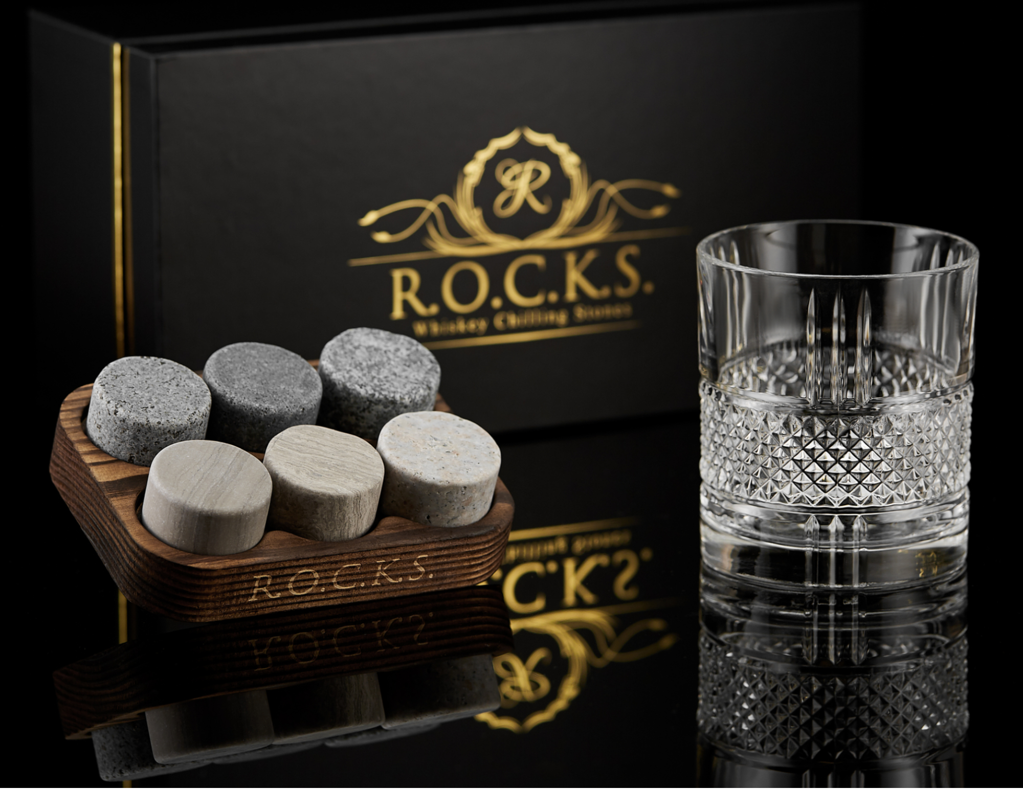 R.O.C.K.S. whiskey stones with a glass and branded box on a reflective surface.